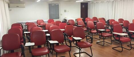 Un aula con filas de sillas y pupitres rojos, paredes blancas y suelo de madera.