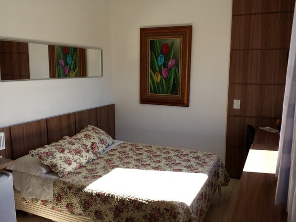 Un dormitorio con cama, mesita de noche, espejo y un cuadro en la pared.