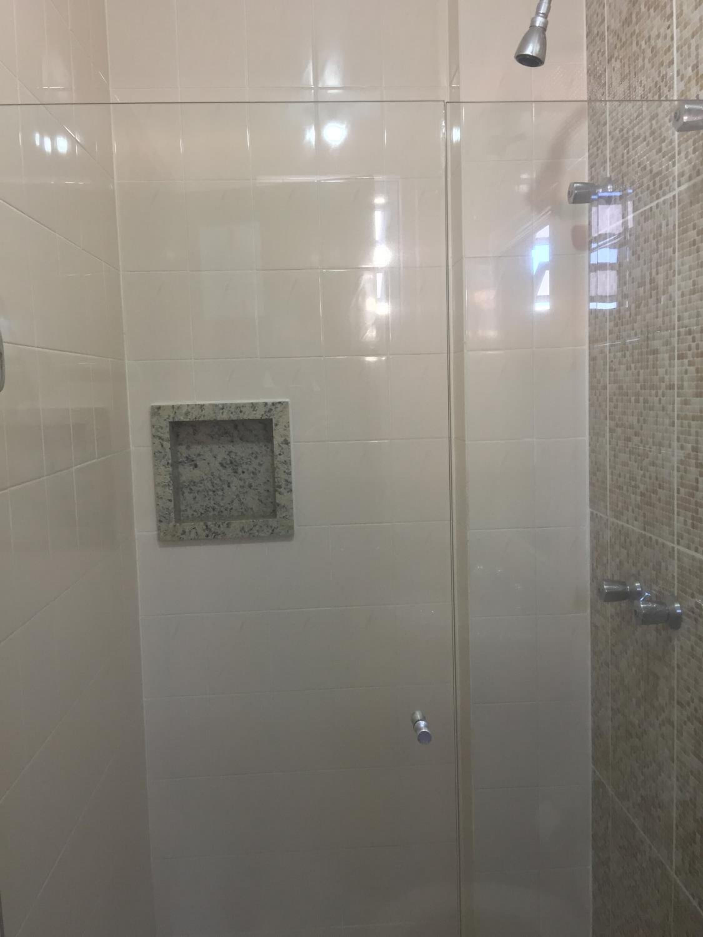 A glass-enclosed shower with white tiles and a small granite accent.
