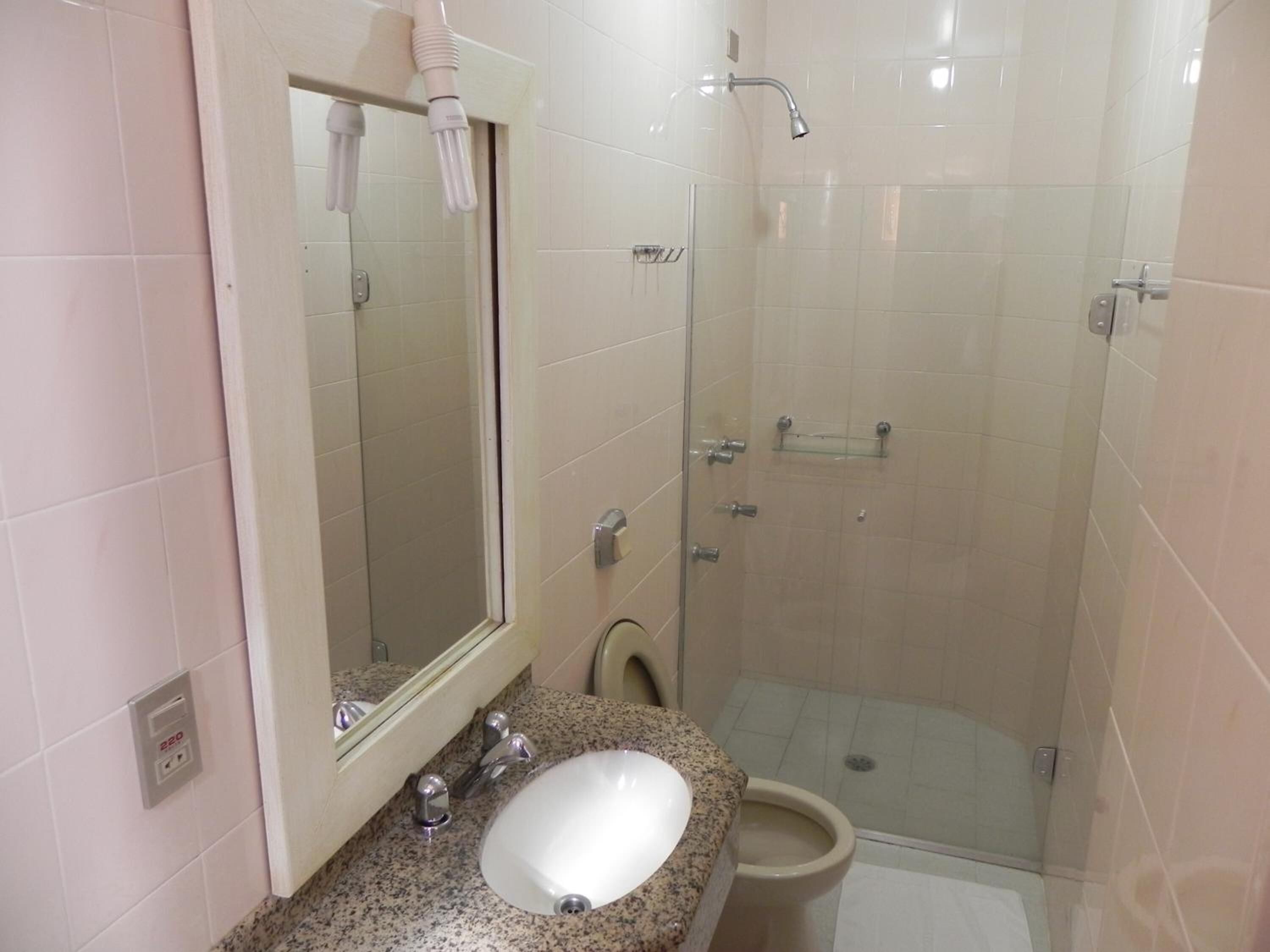 Een badkamer met een wastafel met granieten blad, een spiegel, toilet en een douche met glazen wanden.