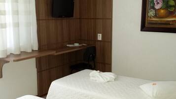 A hotel room with two beds, a TV mounted on the wall, a painting of flowers, and a window with curtains.