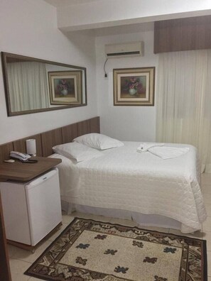 Una habitación de hotel con una cama, un escritorio pequeño con teléfono, y dos cuadros en la pared.