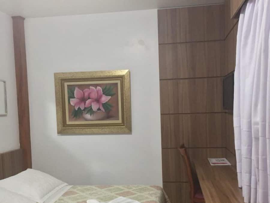 Una habitación de hotel con una cama, un banco de madera, un televisor y un cuadro en la pared.