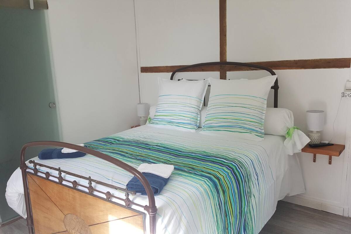 A bed with a wooden frame and a striped bedspread. There is a bedside table with a lamp and a remote control.