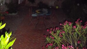 Un edificio de ladrillo con contraventanas blancas, una mesa de vidrio y sillas en el patio.