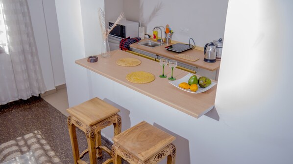 A compact kitchen with a wooden countertop, a sink, a microwave, and a small dining area with two stools.