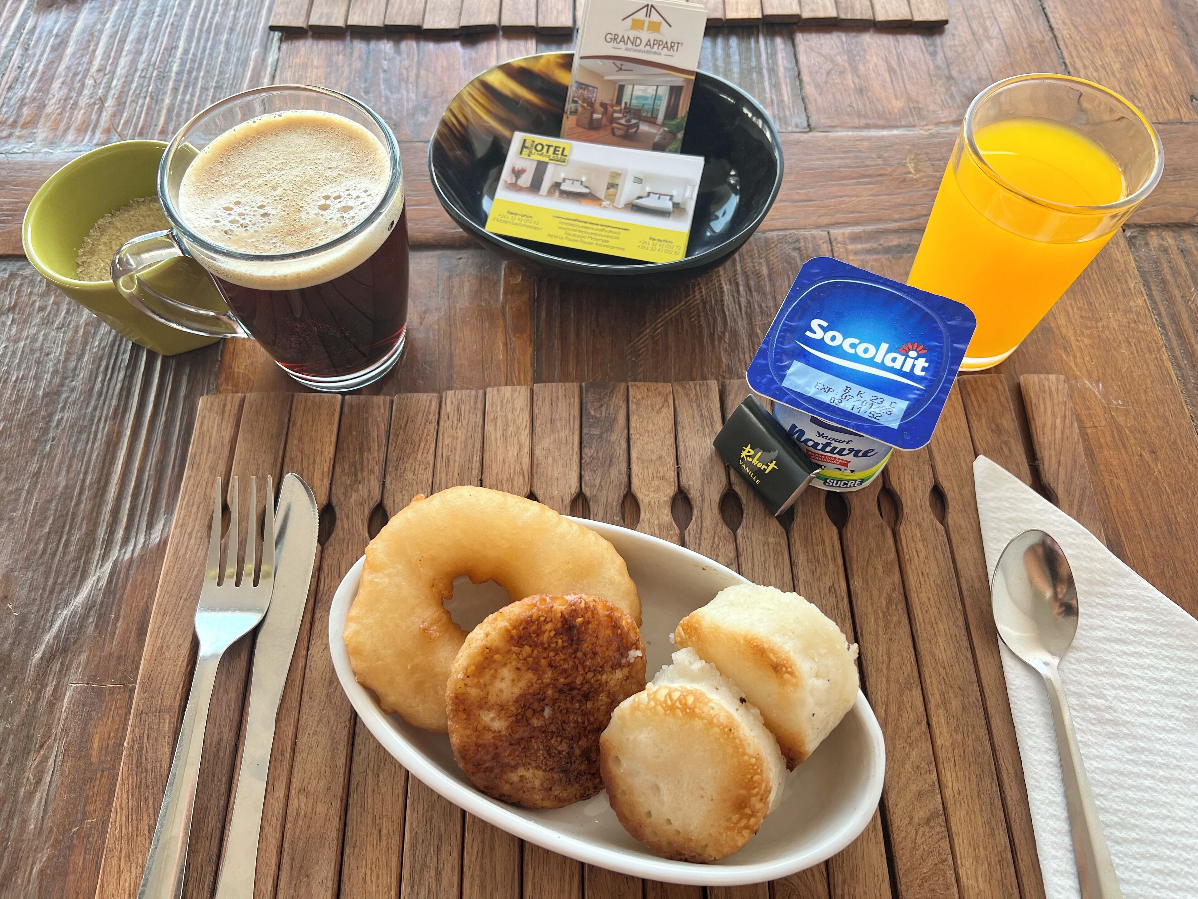 Une table dressée pour le petit-déjeuner avec une assiette de viennoiseries, une tasse de café, un verre de jus d’orange et une brochure d’hôtel.