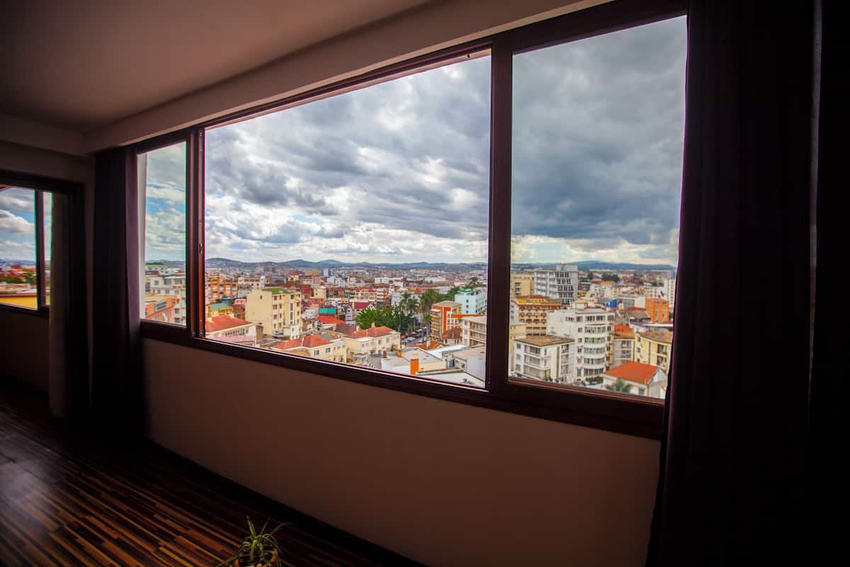 Ein Zimmer mit einem großen Fenster und Blick auf eine Stadtlandschaft mit Gebäuden und bewölktem Himmel.