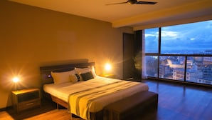 Ein geräumiges Schlafzimmer mit einem großen Bett, einer Bank und einem Nachttisch. Es bietet Blick auf die Stadt durch ein großes Fenster.