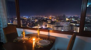 A dining table set with plates and a candle, overlooking a cityscape at night.