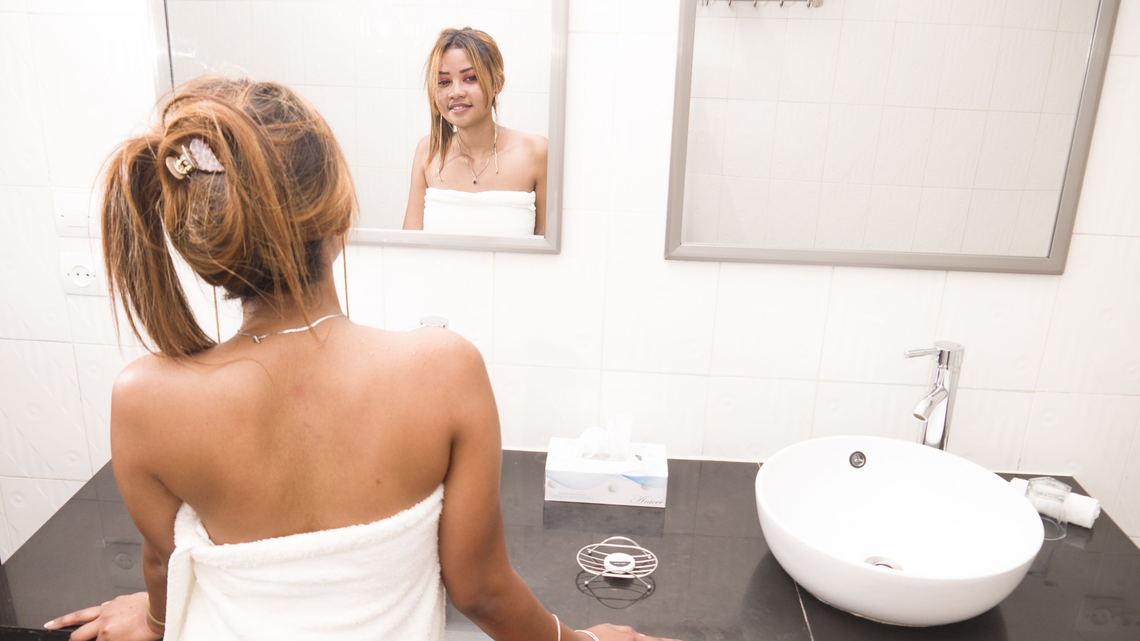 A bathroom with a white sink, a mirror, and a towel hanging on the wall.