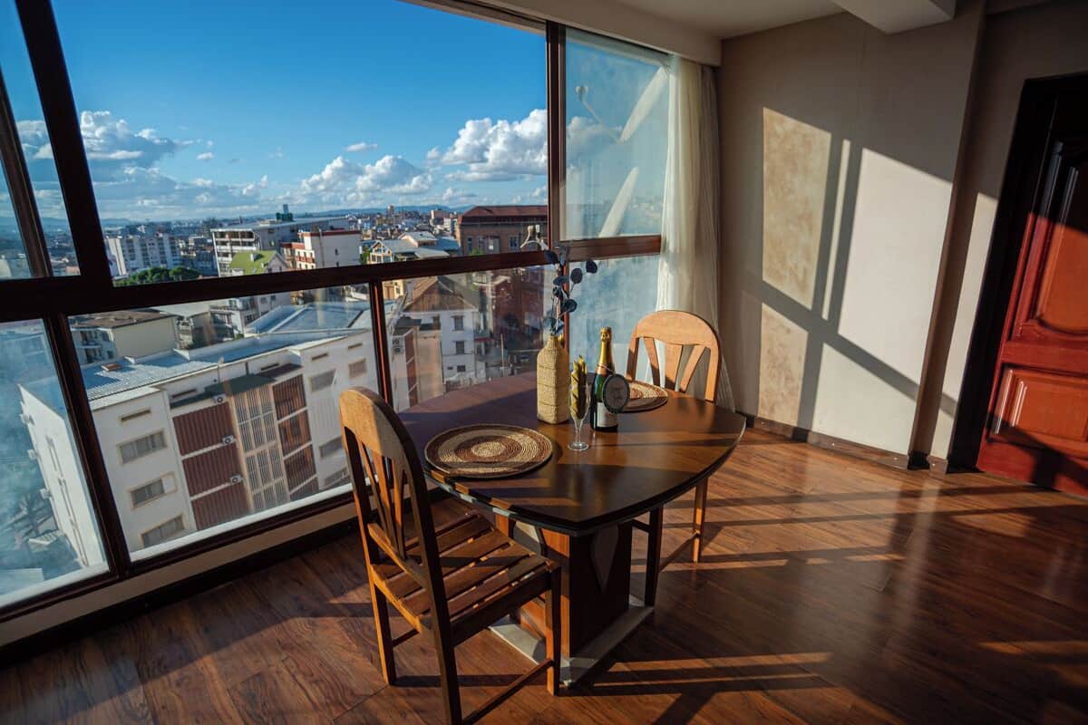 Ein Essbereich mit Tisch und Stühlen, Blick auf eine Stadtlandschaft durch große Fenster und ein Holzboden.