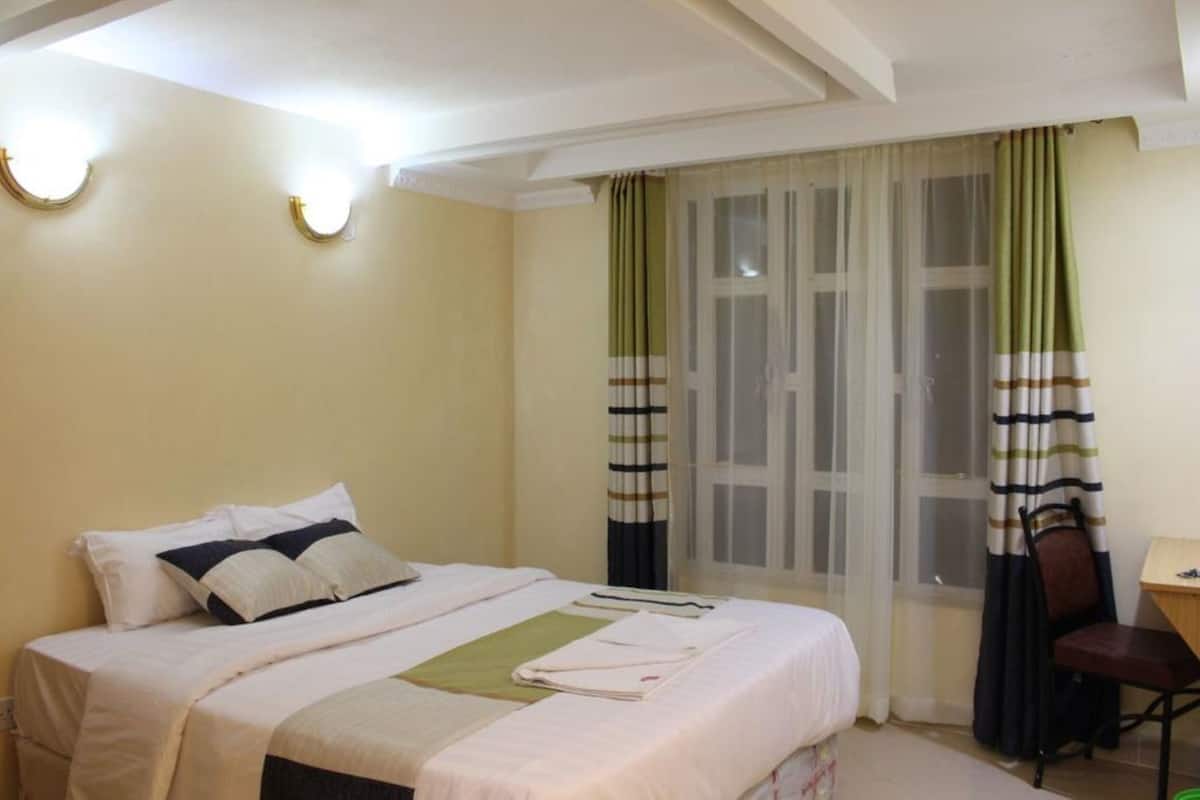 A hotel room with a bed, a chair, a desk, and a window with curtains.