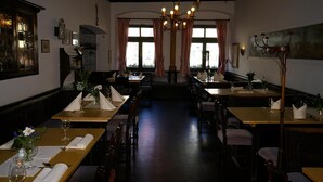 Un restaurante con mesas y sillas de madera, un candelabro y ventanas grandes con cortinas.