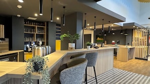 Un moderno bar con una barra de madera, taburetes, iluminación colgante y un piso con diseño de cuadros.