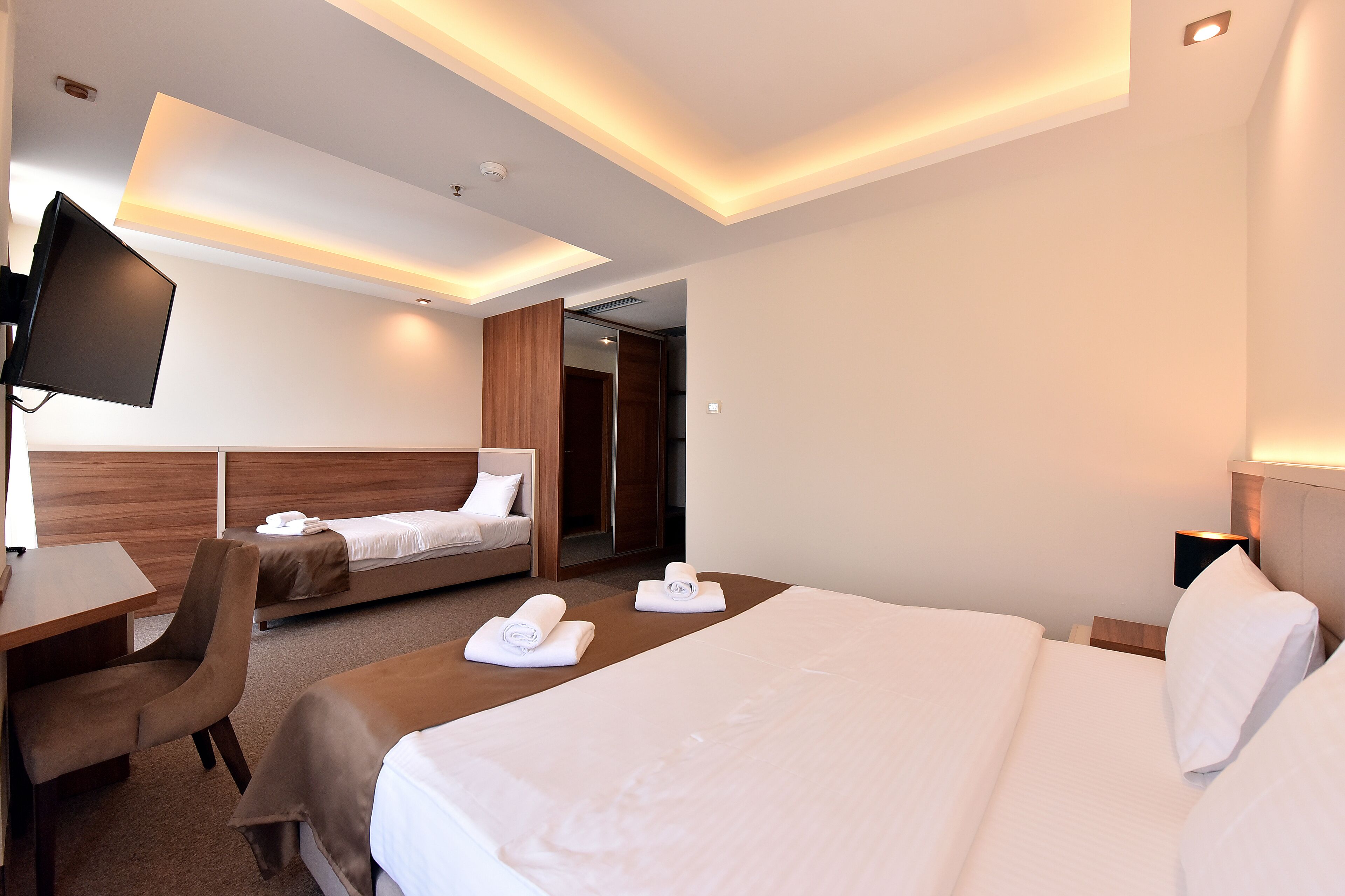A hotel room with a large bed, a desk, a chair, a TV, and a bathroom visible through an open door.