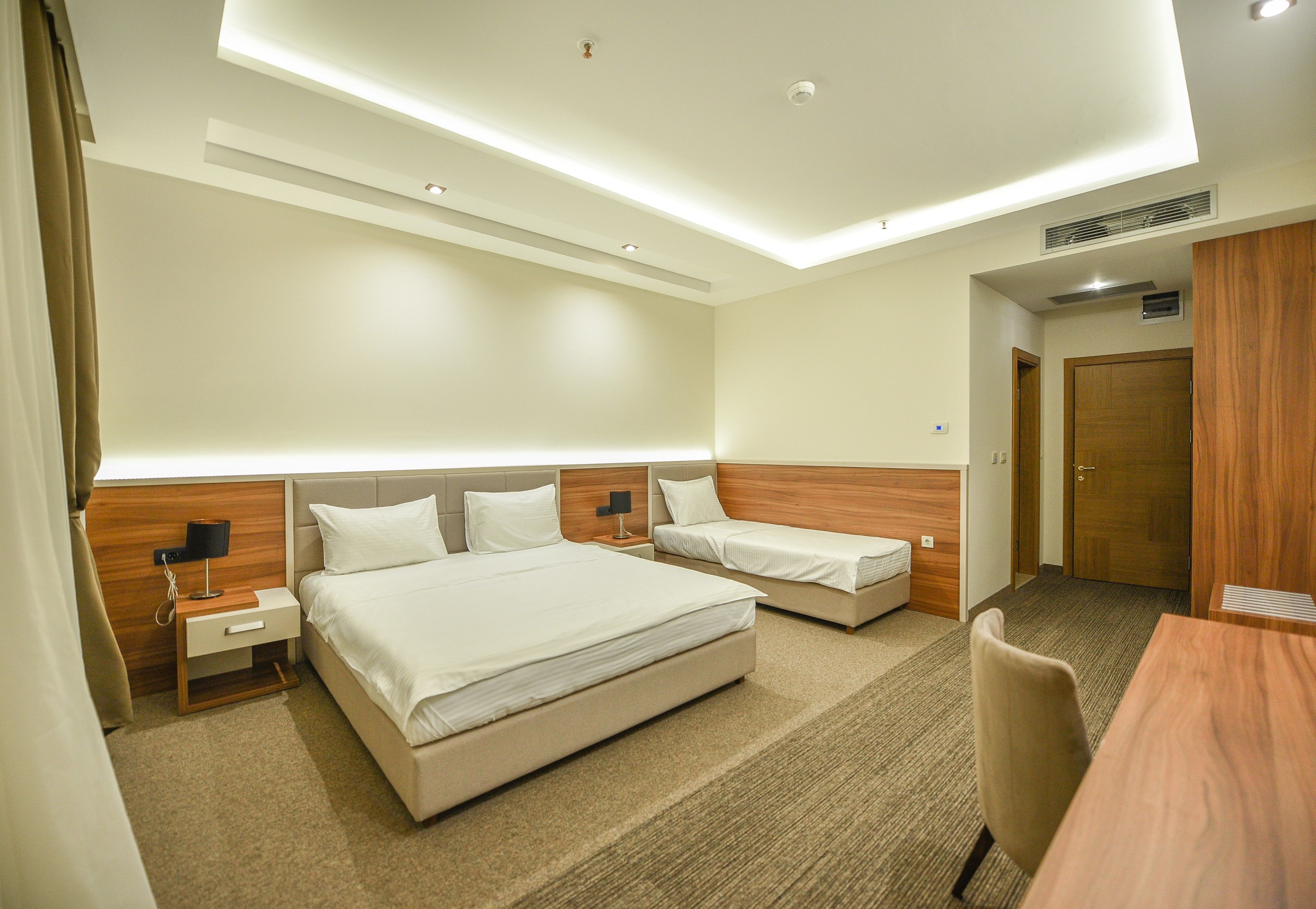 A hotel room with two beds, a desk, a chair, and a wooden wardrobe.