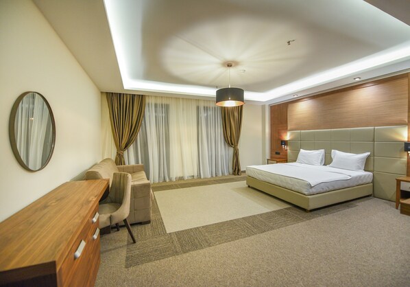 A modern hotel room with a large bed, a desk, a chair, and a ceiling light.