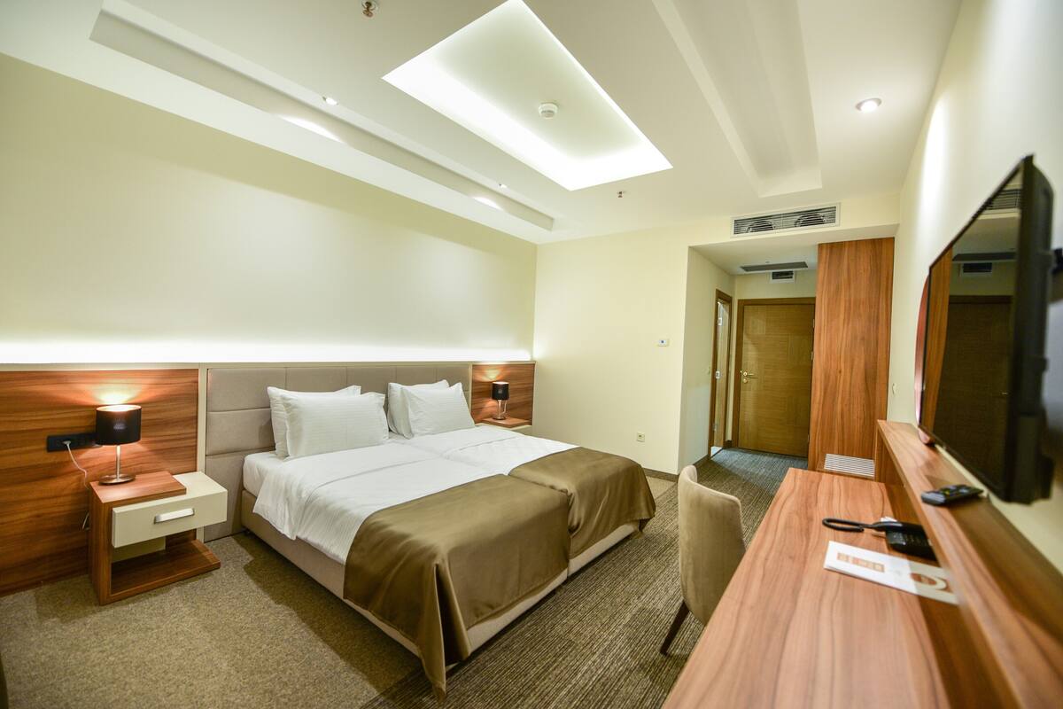 Habitación de hotel con cama, mesitas de noche, escritorio, silla, televisor y espejo.