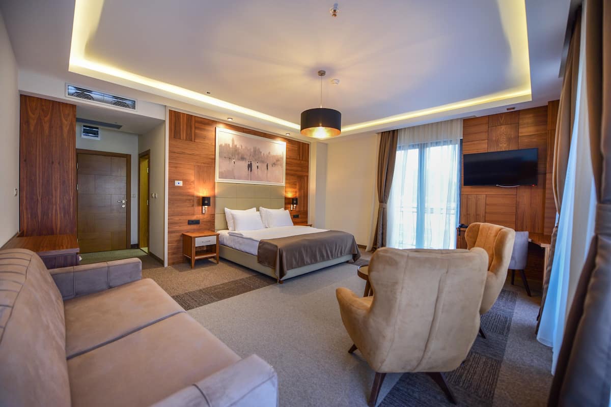 Una habitación de hotel moderna con cama, sofá, sillón, televisor y una pared de acento de madera.
