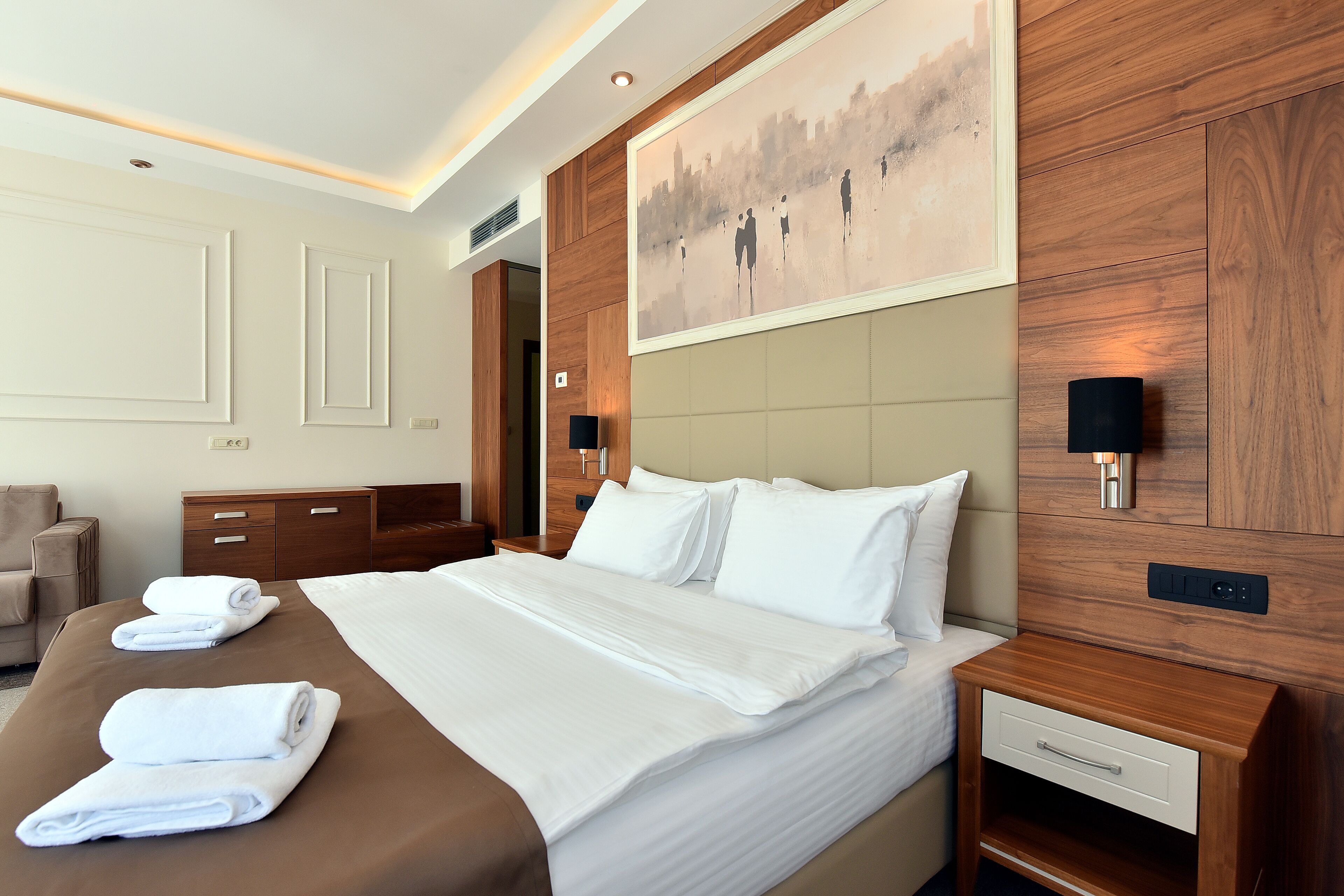 Une chambre d’hôtel avec un grand lit, une tête de lit en bois, un tableau et une table de chevet avec une lampe.