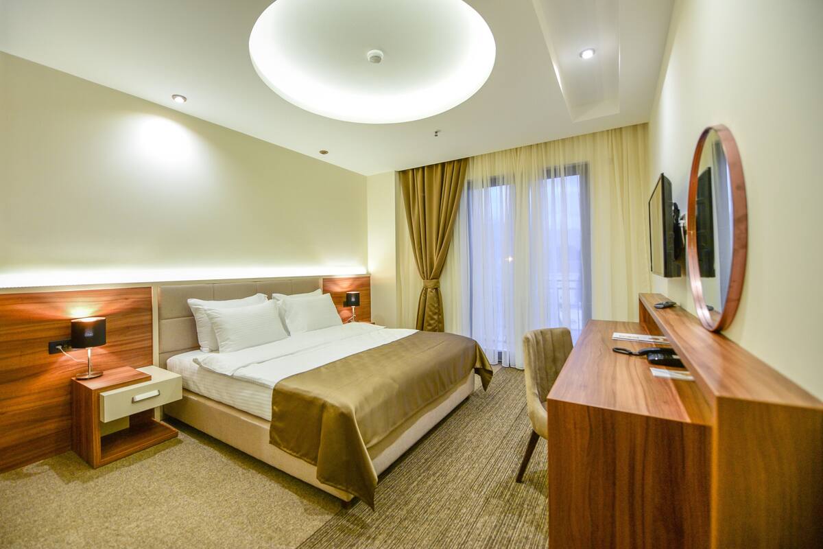 Habitación de hotel con una cama grande, lámparas de noche, un escritorio con espejo y vistas al exterior a través de la ventana.