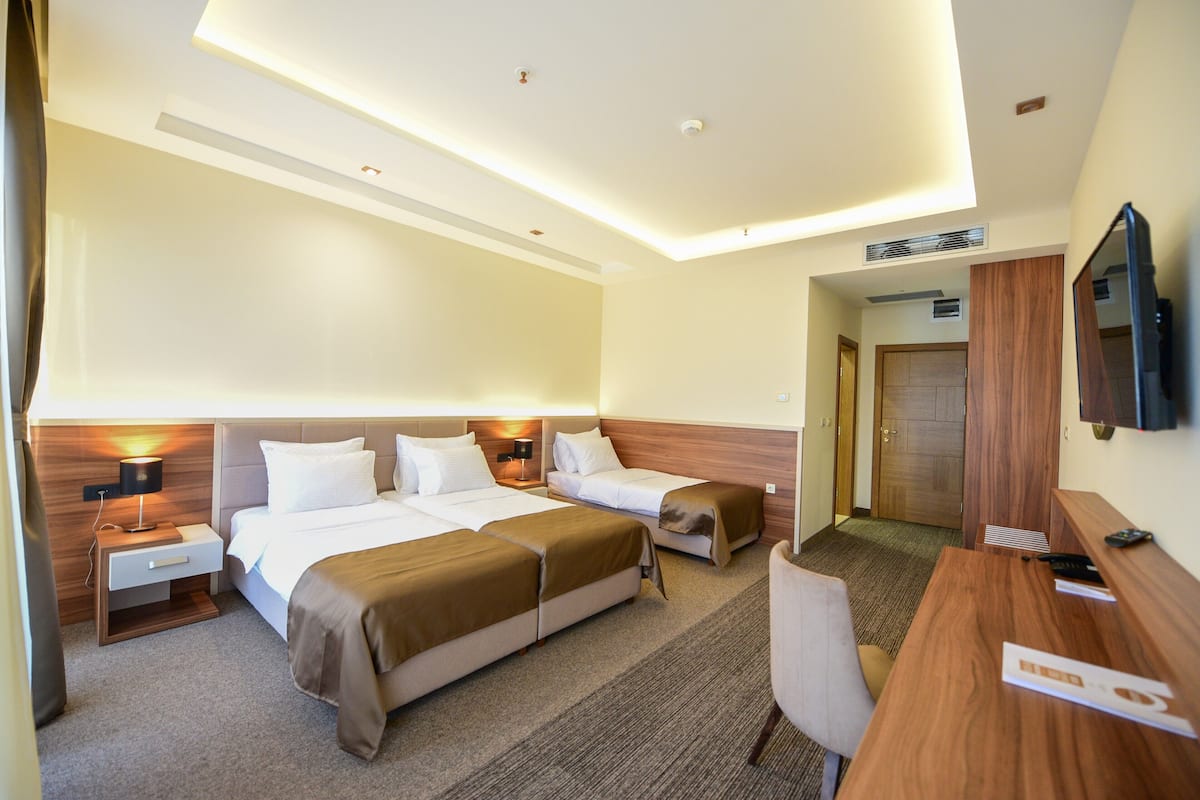 Habitación de hotel con dos camas, un escritorio, una silla, un televisor y una puerta.