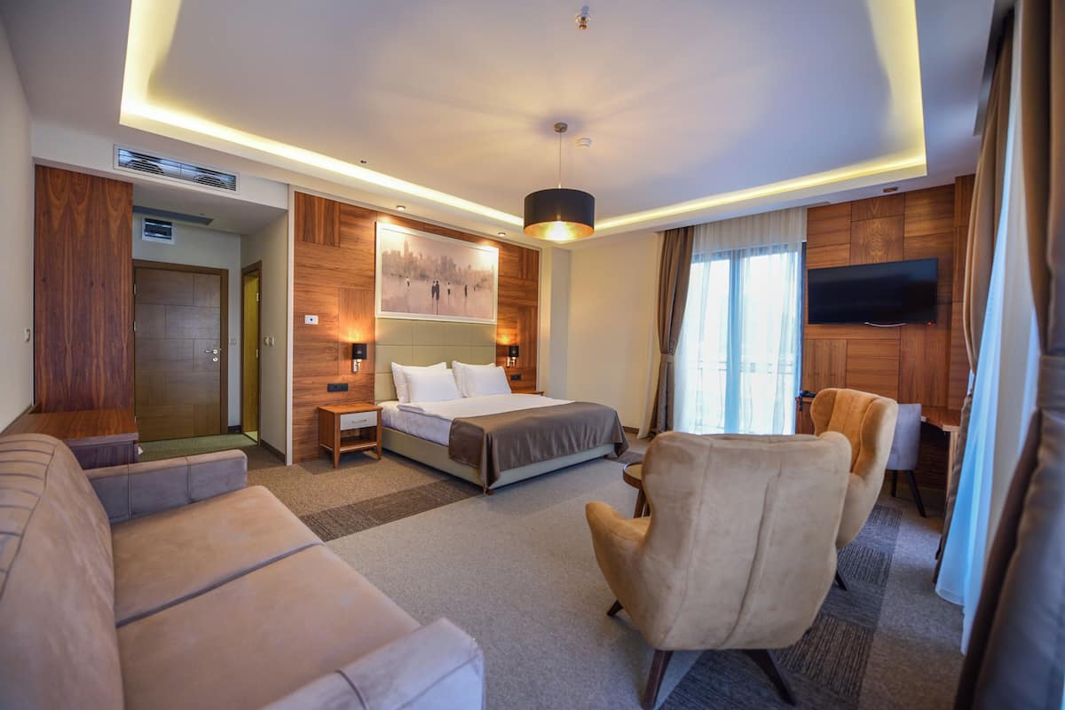 Una habitación de hotel moderna con cama, sofá, sillón, televisor y una pared de acento de madera.