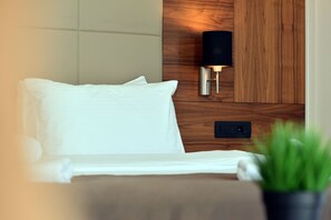 A neatly made bed with white linens, a wall-mounted light fixture, and a small potted plant. - Hotel Lazaro (Podgorica)