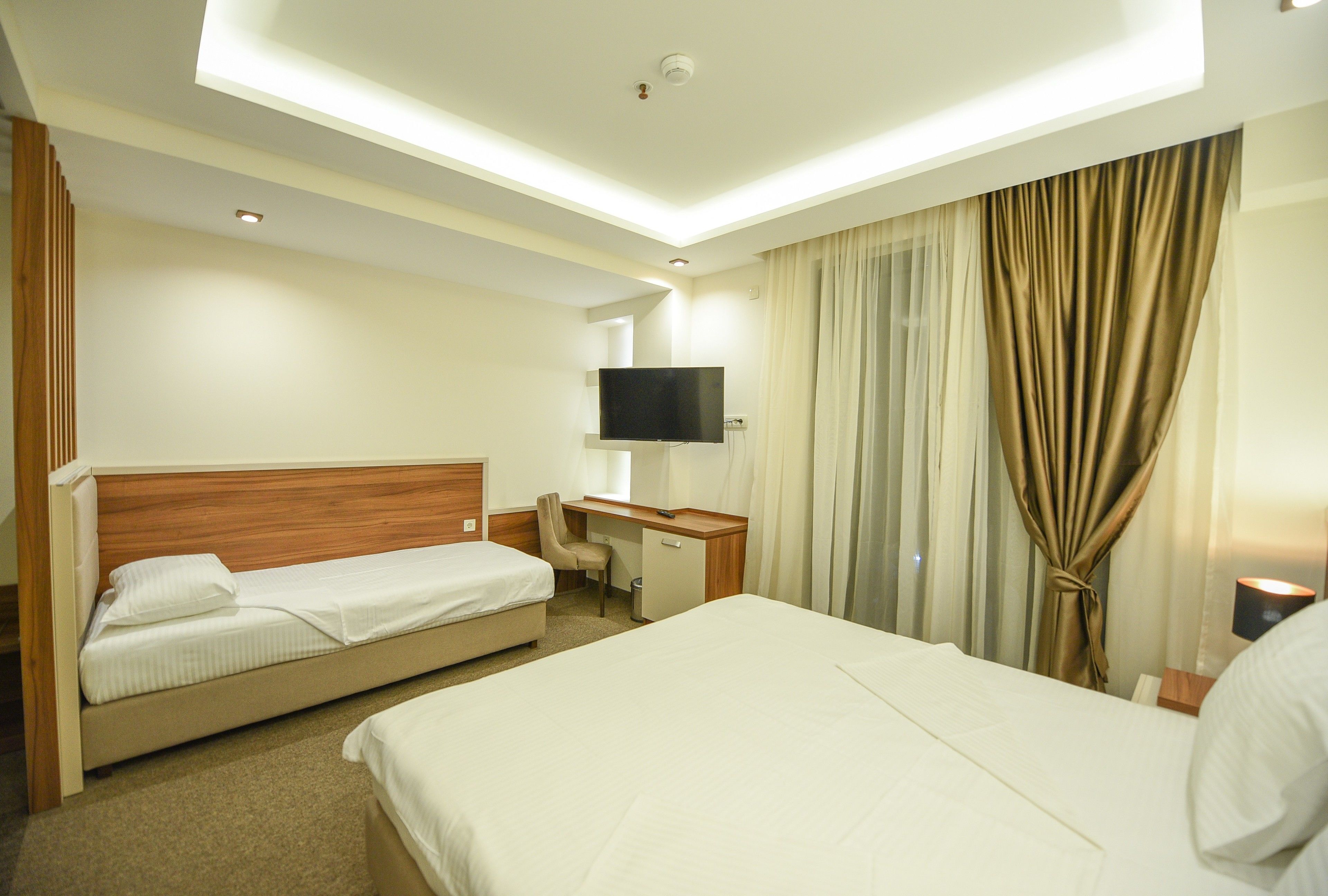 A hotel room with two beds, a desk, a TV, and a window with curtains.