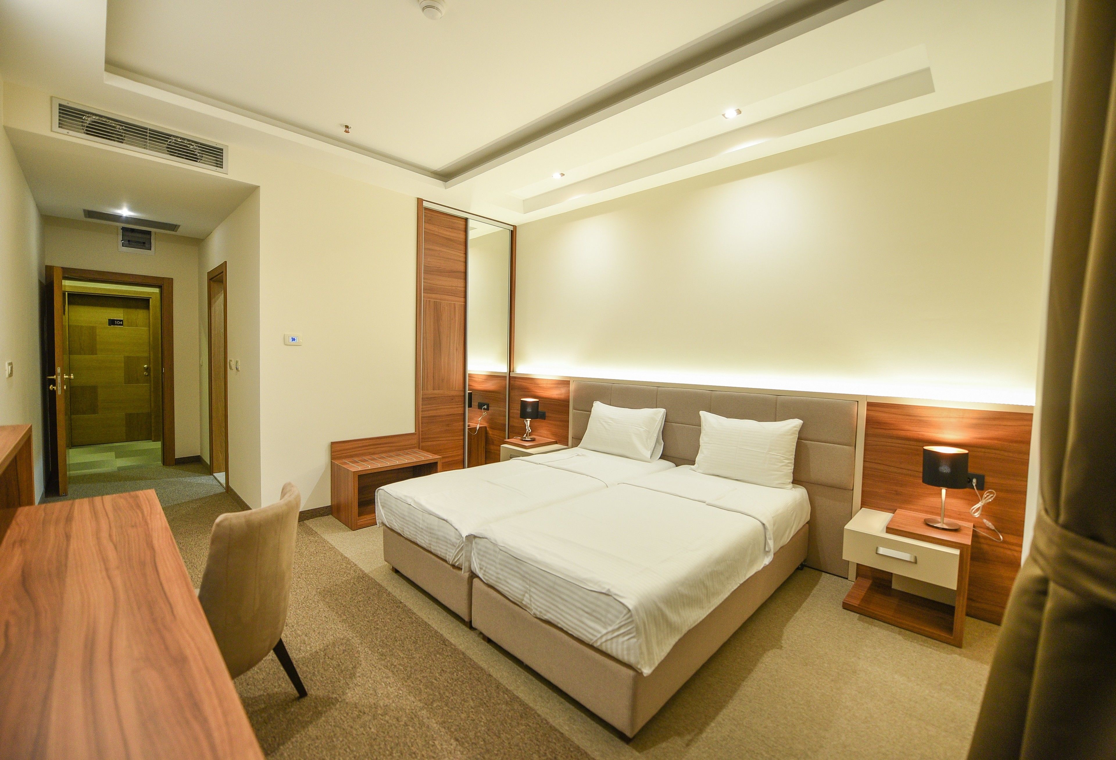 Una habitación de hotel con una cama grande, mesitas de noche, un escritorio y un espejo.