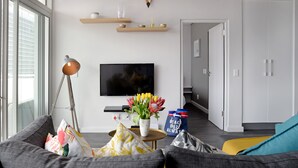 A modern living room with a sofa, a coffee table, a TV, and a vase of flowers. - Zara By Stay Amazing (Cape Town)
