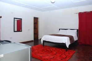 Quarto com cama, tapete vermelho, espelho e porta de madeira.