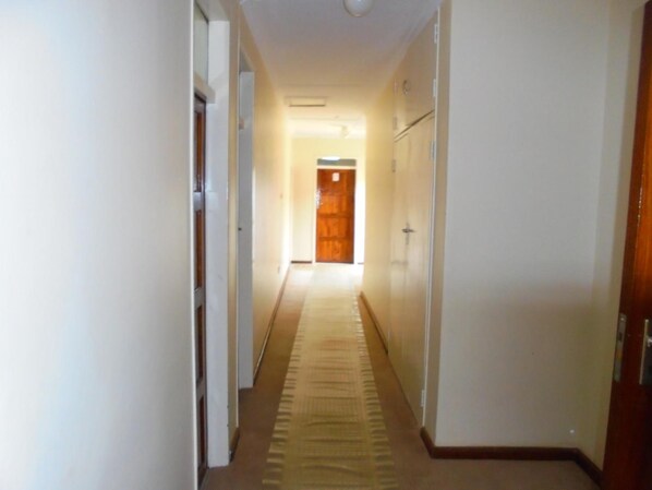 A narrow hallway with a carpeted floor, white walls, and a wooden door at the end.