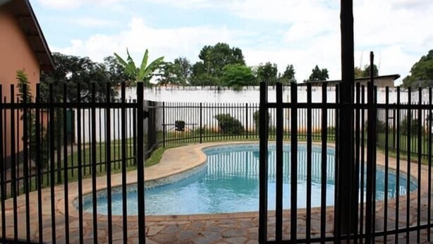 A swimming pool surrounded by a stone patio and a black metal fence. - Sharon's Guest House (Lusaka)