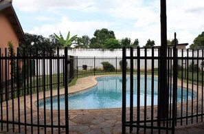 A swimming pool surrounded by a stone patio and a black metal fence.