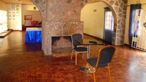 A room with a stone fireplace, wooden flooring, and two chairs. - Sharon's Guest House (Lusaka)