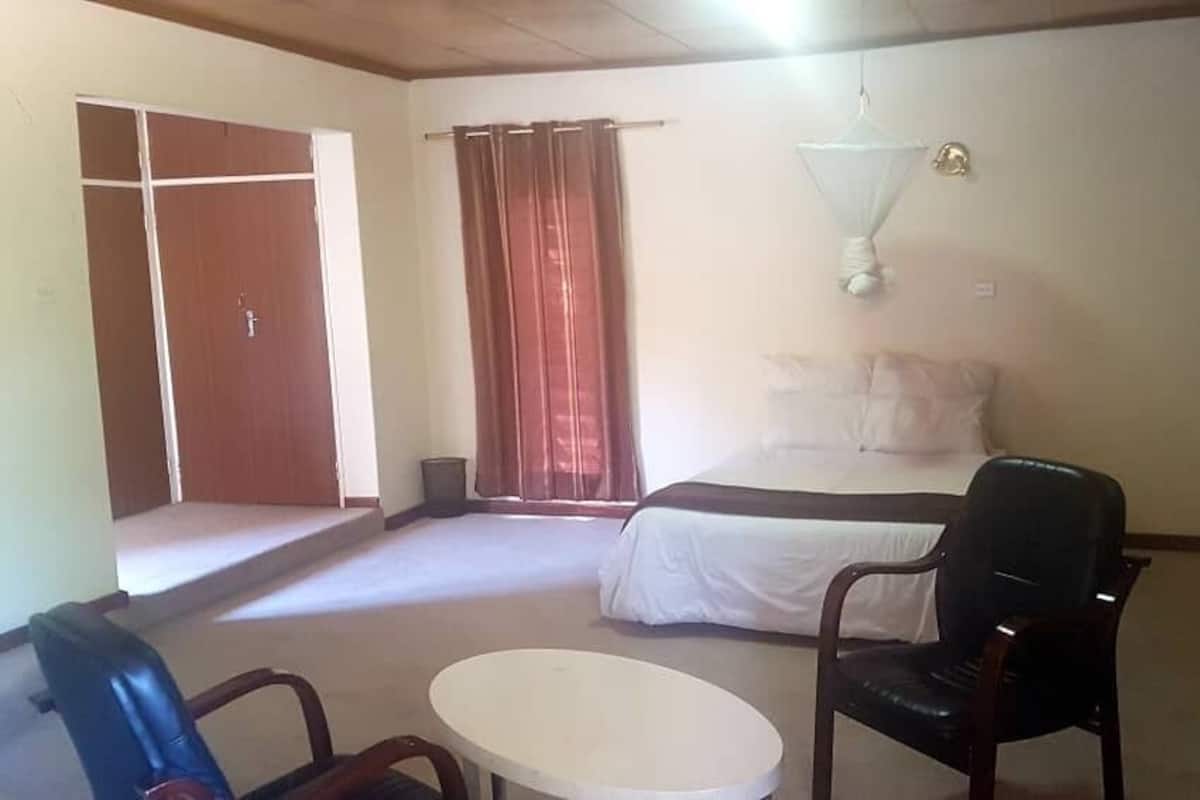 A room with a bed, a chair, a table, a wardrobe, and a window with curtains.