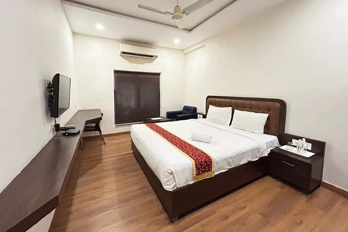 Una habitación de hotel moderna con una cama grande, un escritorio, una silla, un televisor, un ventilador de techo y una ventana con persiana.