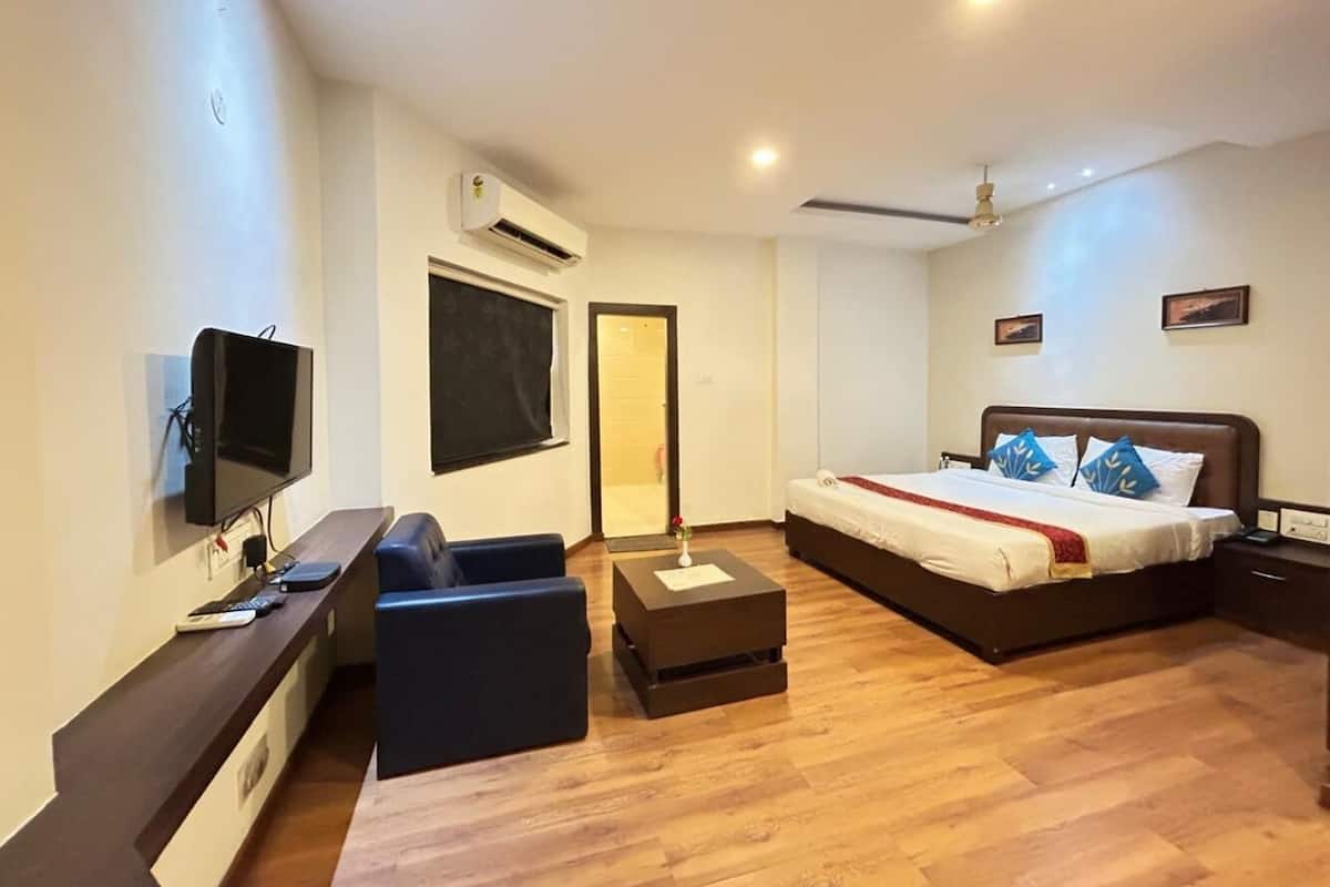 Una habitación de hotel moderna con un televisor de pantalla plana, un sofá, una cama con una manta roja y suelo de madera.