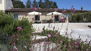 Un bâtiment en pierre, avec deux parasols blancs, entouré de plantes et d’arbres en fleurs.