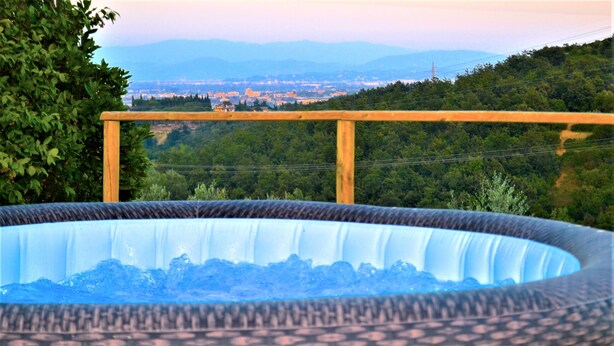 Un bain à remous entouré d’une terrasse en bois, avec vue sur une ville et des montagnes en arrière-plan.