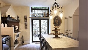 Une cuisine avec un mur en pierre, un grand îlot central agrémenté d’un élément décoratif, et un coin repas avec des chaises.