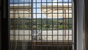 Une vue à travers une fenêtre avec des barreaux en métal, où l’on aperçoit des parasols et une chaise à l’extérieur.