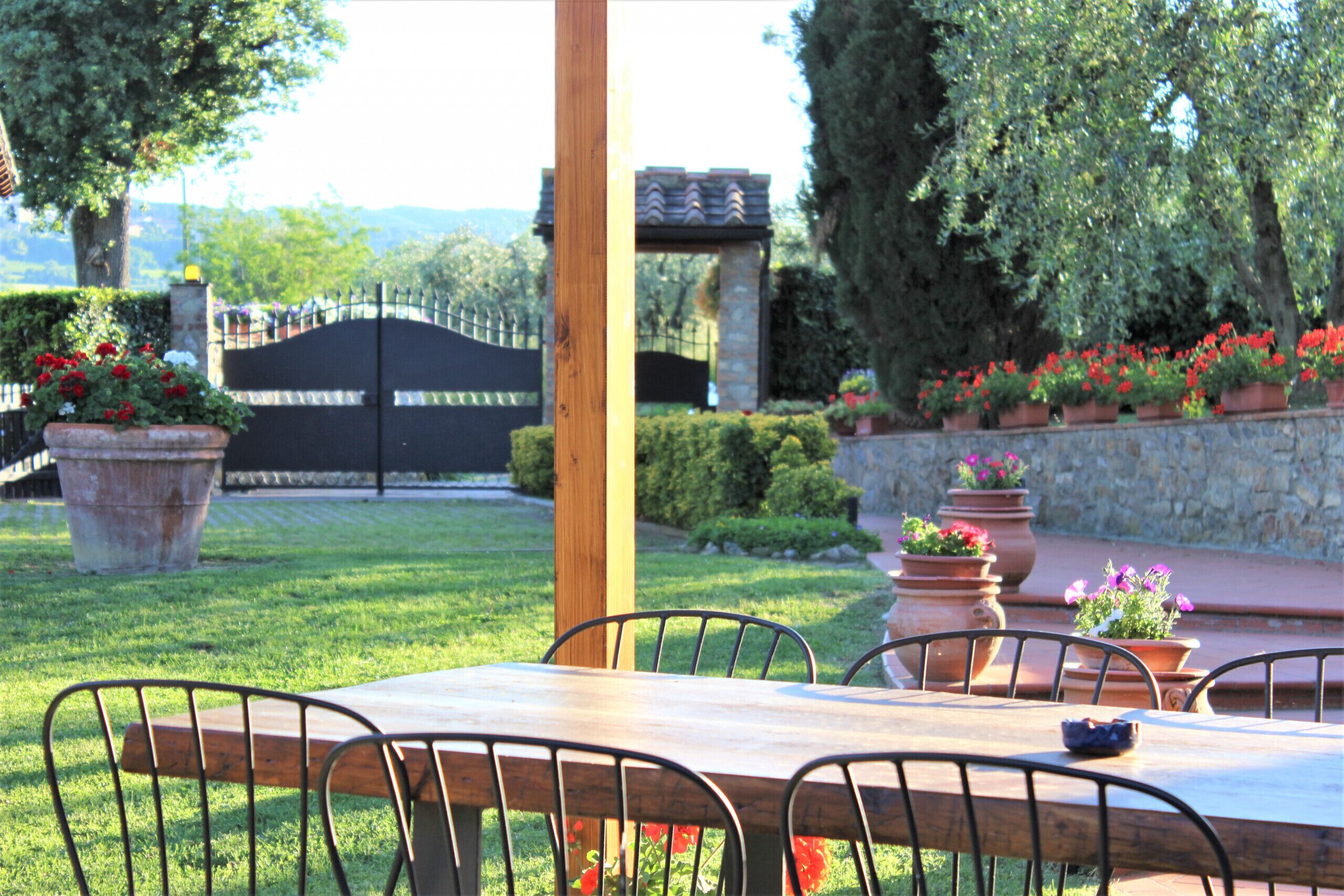 An outdoor dining area with a wooden table and metal chairs, surrounded by potted plants and a stone wall.
