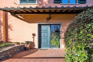 A building with a blue door, a small porch with potted plants, and a wall-mounted light fixture.