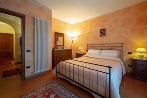 A bedroom with a bed, bedside tables, a nightstand, a radiator, a door, and a wall-mounted picture.