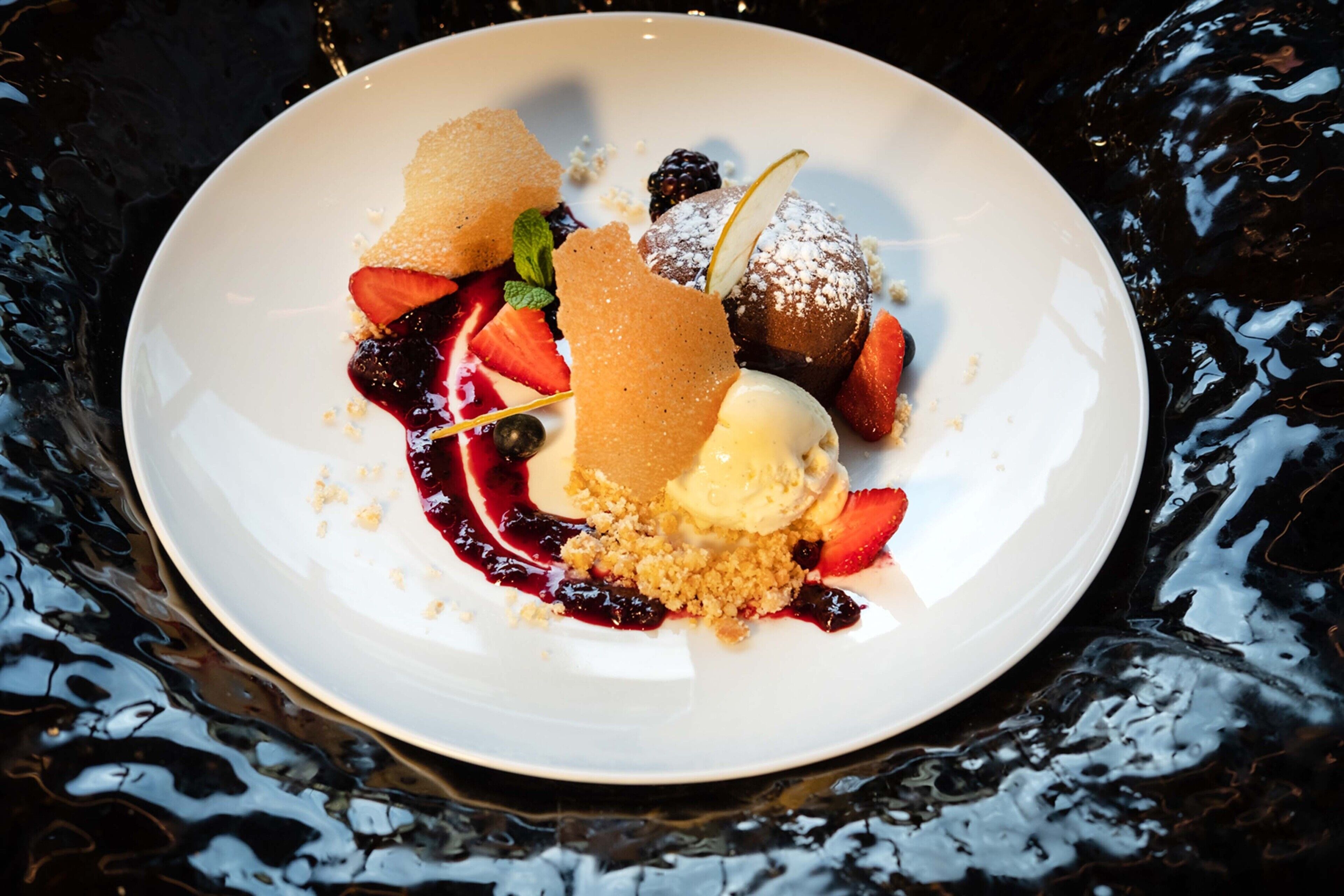 Un plato de postre con diversas frutas y una bola de helado.