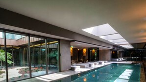 A modern indoor swimming pool with glass walls, a skylight, and a view of a garden.
