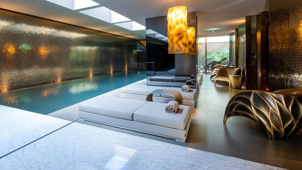 A modern indoor pool area with a glass wall, lounge seating, and a unique light fixture.